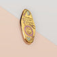 A Health Worker's Talisman gold enamel pin on a gold foiled backing card that outlines the symbolism of the talisman including information and imagery on the Rod of Asclepius, Lavender Stems and Prehnite Crystals