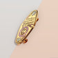 A Health Worker's Talisman gold enamel pin on a gold foiled backing card that outlines the symbolism of the talisman including information and imagery on the Rod of Asclepius, Lavender Stems and Prehnite Crystals