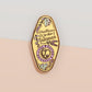 A Health Worker's Talisman gold enamel pin on a gold foiled backing card that outlines the symbolism of the talisman including information and imagery on the Rod of Asclepius, Lavender Stems and Prehnite Crystals