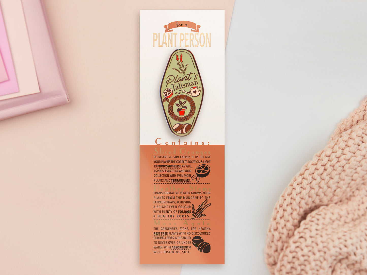 A Plant Person's Talisman gold enamel pin on a gold foiled backing card that outlines the symbolism of the talisman including information and imagery on sliced oranges, heather stems, and moss agate