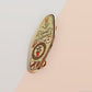 A Plant Person's Talisman gold enamel pin on a gold foiled backing card that outlines the symbolism of the talisman including information and imagery on sliced oranges, heather stems, and moss agate