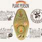 A detailed illustration outlining the symbolism of the Plant Person's Talisman gold enamel pin on a gold foiled backing card that outlines the symbolism of the talisman