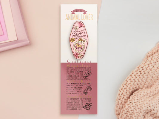 An Animal Lover's Talisman gold enamel pin on a gold foiled backing card that outlines the symbolism of the talisman including information and imagery on Magnolia flowers, yellow roses, and aragonite star clusters