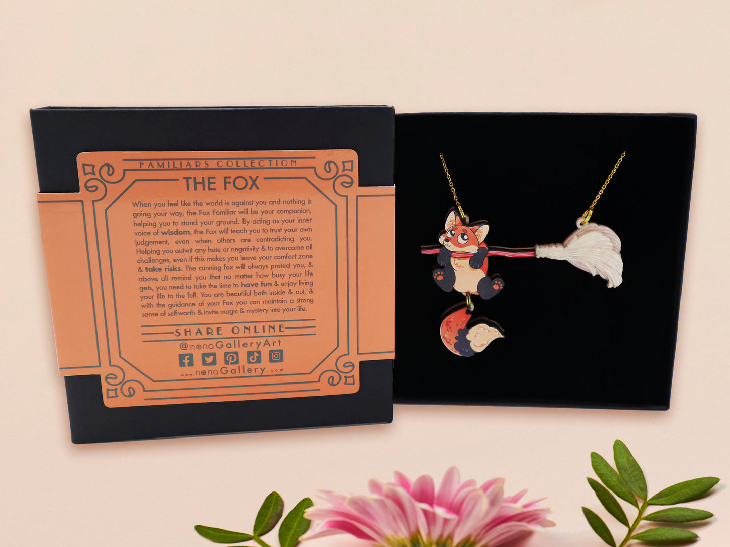 Mixed material handmade necklace of chibi cartoon Fox hanging on to a pearlescent witches broomstick, with a gold chain and black gift box with an orange familiars collection gift sleeve.