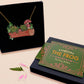 A wooden and glitter acrylic necklace with gold chain in a black box of two cute frogs sat on a log smiling surrounded by flowers, plants and mushrooms