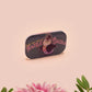 A clear acrylic pin badge with a pink heart-shaped pin back clasp. The design of the pin badge is of a cute chibi penguin dancing in a suit under a spotlight with the quote give 'em the ol' razzle dazzle