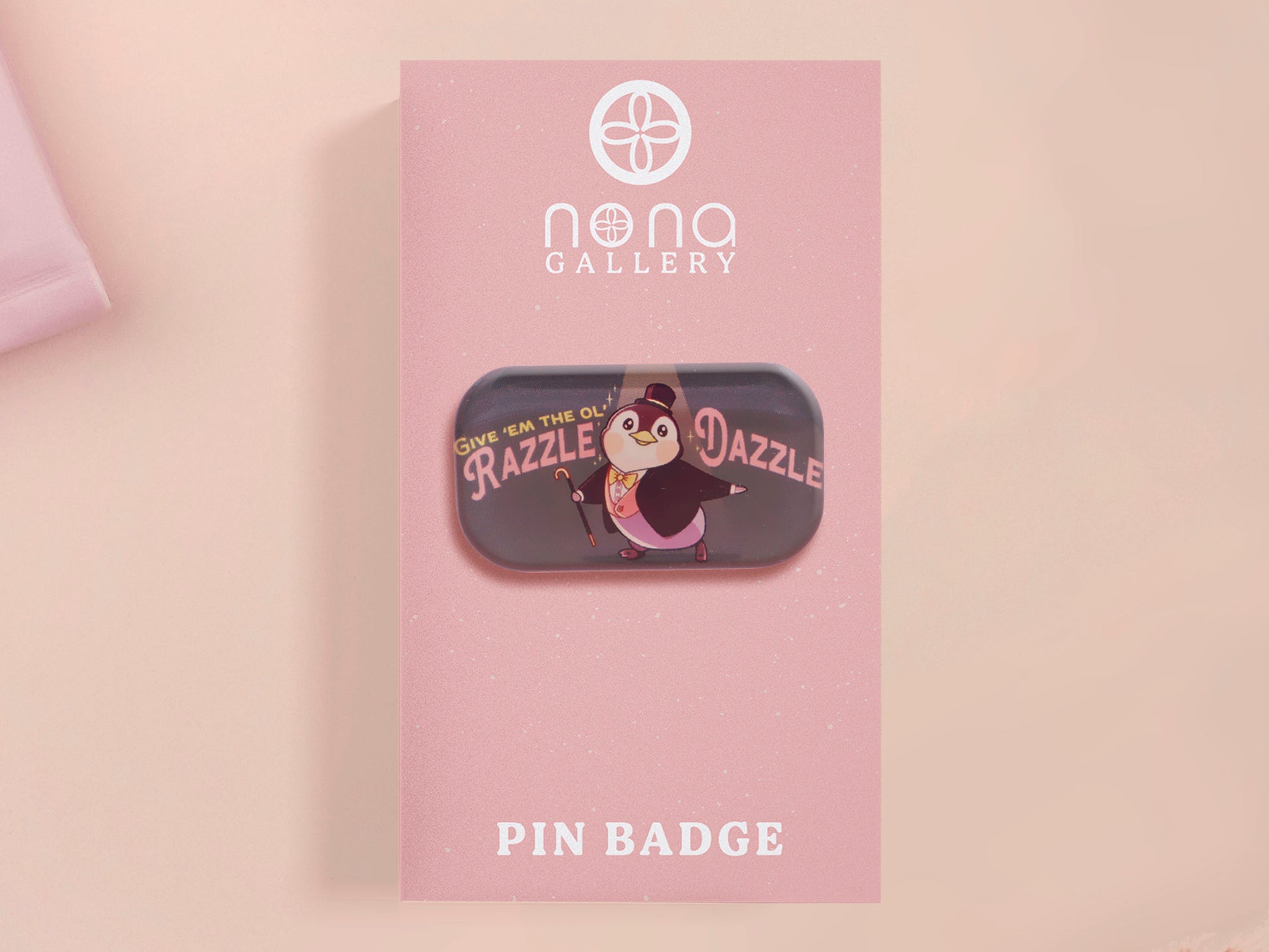 A clear acrylic pin badge with a pink heart-shaped pin back clasp. The design of the pin badge is of a cute chibi penguin dancing in a suit under a spotlight with the quote give 'em the ol' razzle dazzle