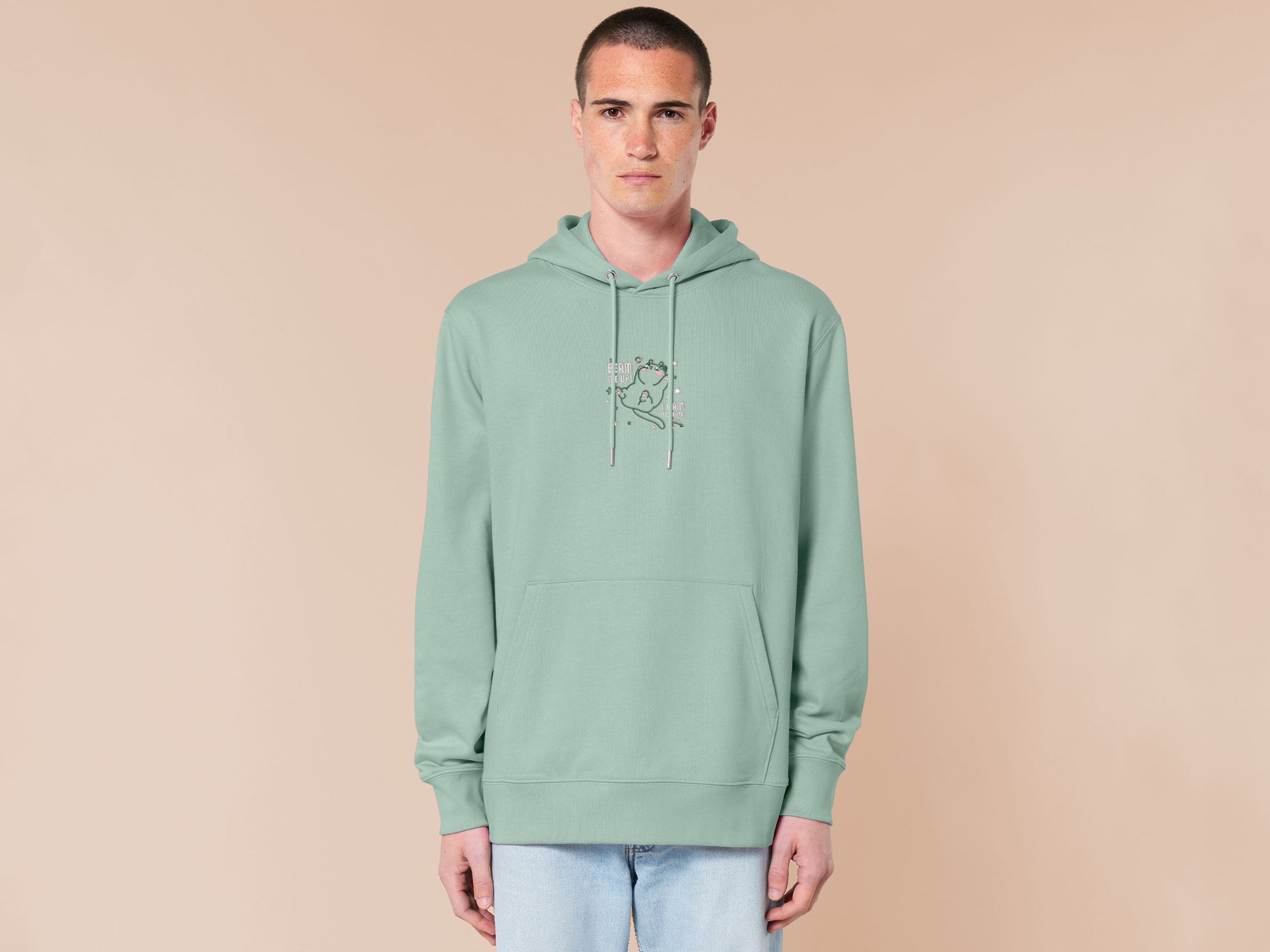 An embroidered green hoodie design of a cute alien cat floating in space surrounded by stars and planets and by the quote beam me up! I want to leave