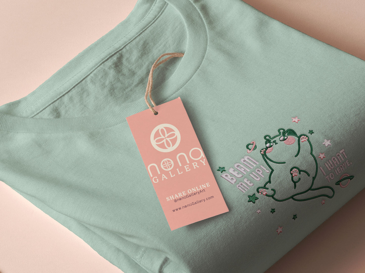 An embroidered green t-shirt design of a cute alien cat floating in space surrounded by stars and planets and by the quote beam me up! I want to leave