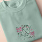 An embroidered green t-shirt design of a cute alien cat floating in space surrounded by stars and planets and by the quote beam me up! I want to leave