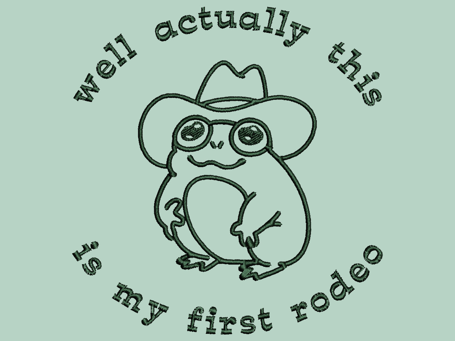 An embroidered green t-shirt design of a cute cowboy frog wearing a stetson surrounded by the test well actually this is my first rodeo.