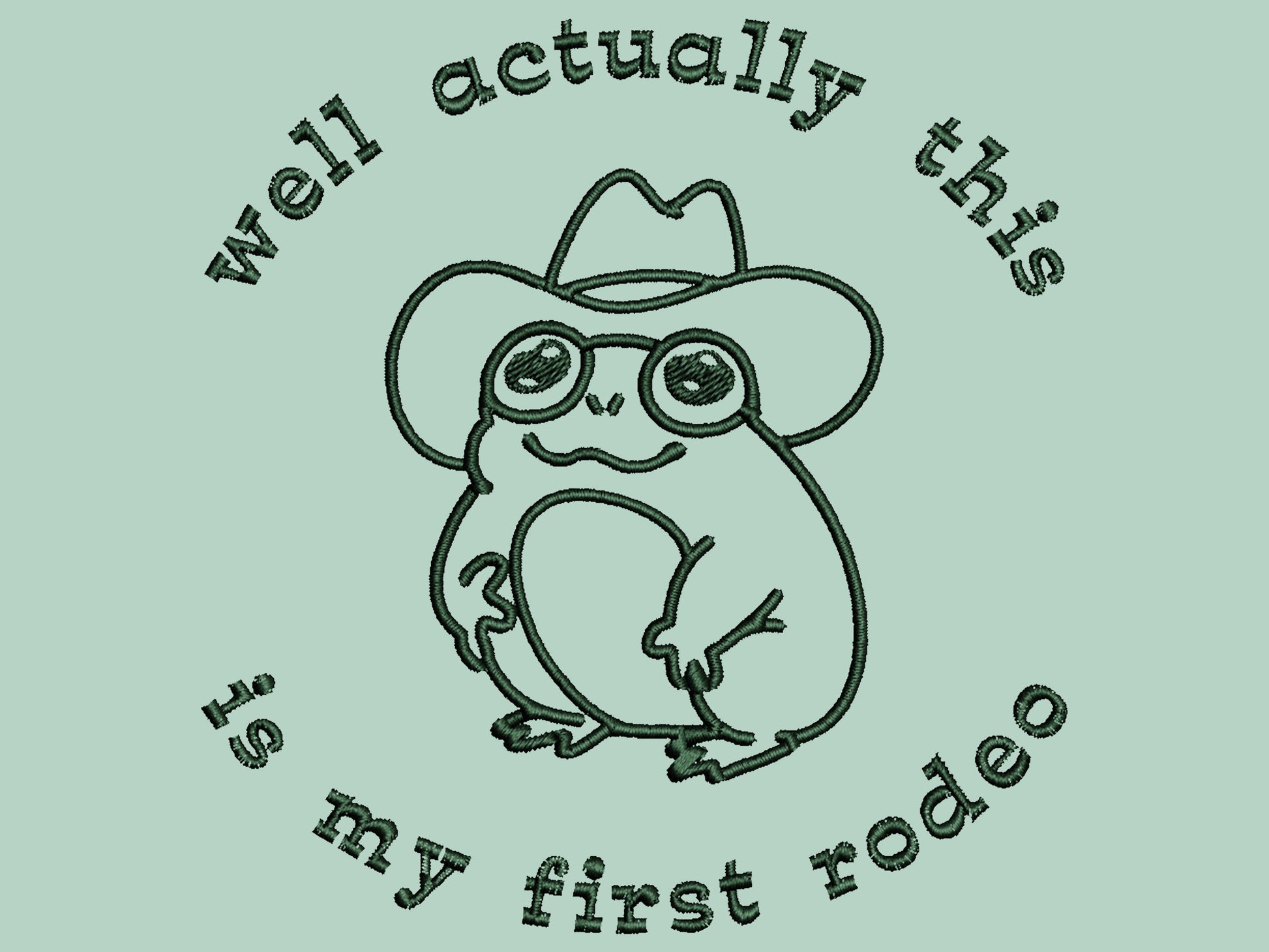 An embroidered green t-shirt design of a cute cowboy frog wearing a stetson surrounded by the test well actually this is my first rodeo.