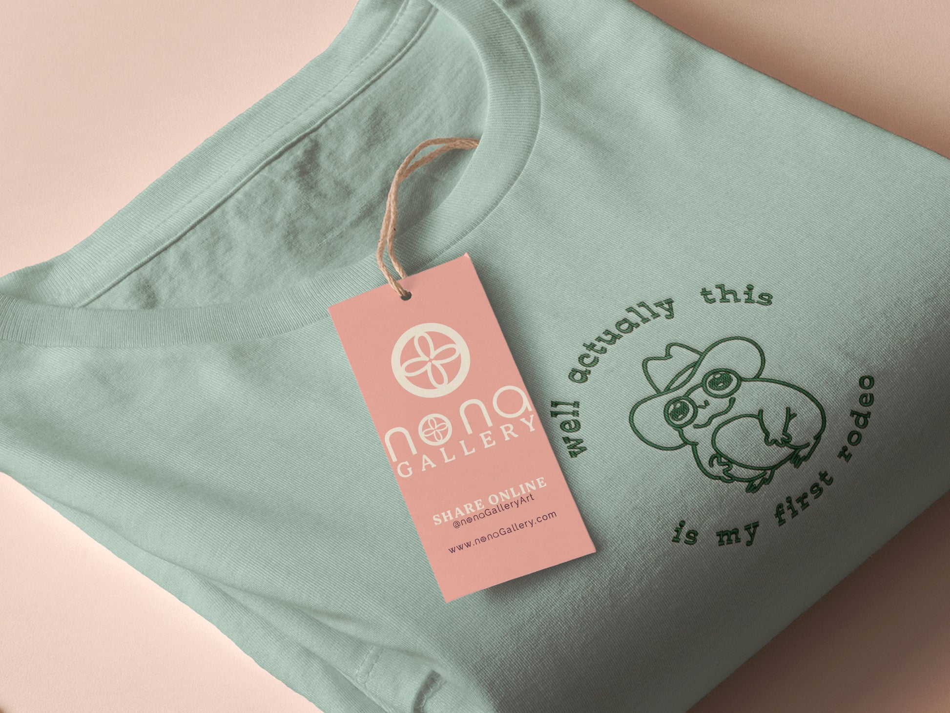 An embroidered green t-shirt design of a cute cowboy frog wearing a stetson surrounded by the test well actually this is my first rodeo.