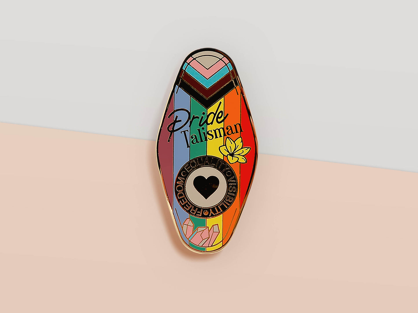 Gold Enamel Talisman Pin with progress pride flag design and the words Pride Talisman, Freedom Equality Visibility. The pins design includes a heart, flowers and crystals.