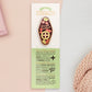 The Strength Talisman gold enamel pin on a gold foiled backing card that outlines the symbolism of the talisman including information and imagery on the Tabono adinkra Symbol, potential flowers, and chrysoprase stones