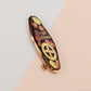 The Strength Talisman gold enamel pin on a gold foiled backing card that outlines the symbolism of the talisman including information and imagery on the Tabono adinkra Symbol, potential flowers, and chrysoprase stones