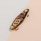 The Strength Talisman gold enamel pin on a gold foiled backing card that outlines the symbolism of the talisman including information and imagery on the Tabono adinkra Symbol, potential flowers, and chrysoprase stones