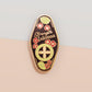 The Strength Talisman gold enamel pin on a gold foiled backing card that outlines the symbolism of the talisman including information and imagery on the Tabono adinkra Symbol, potential flowers, and chrysoprase stones