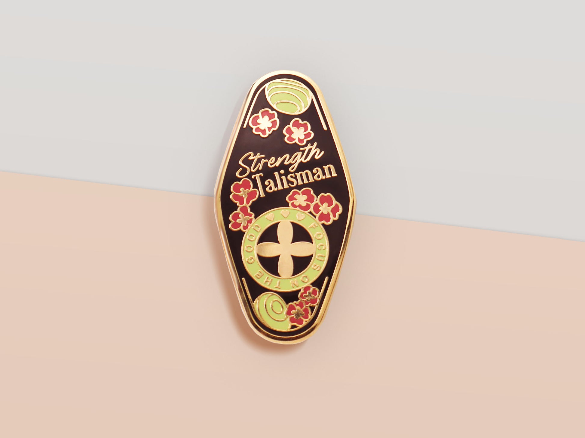 The Strength Talisman gold enamel pin on a gold foiled backing card that outlines the symbolism of the talisman including information and imagery on the Tabono adinkra Symbol, potential flowers, and chrysoprase stones