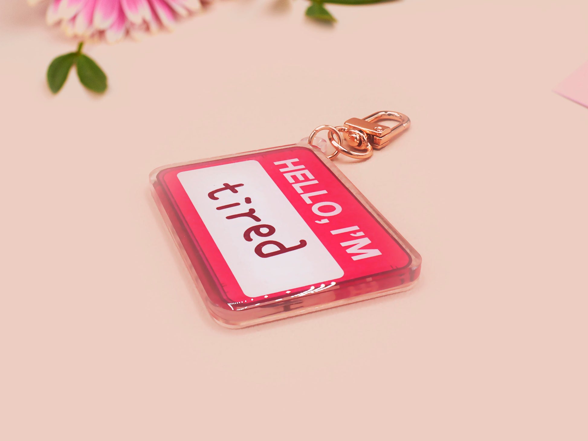 Multiple acrylic keychains with gold swivel clasps in the hello I'm name badge style with the word tired written instead of a name