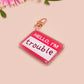 Multiple acrylic keychains with gold swivel clasps in the hello I'm name badge style with the word trouble written instead of a name
