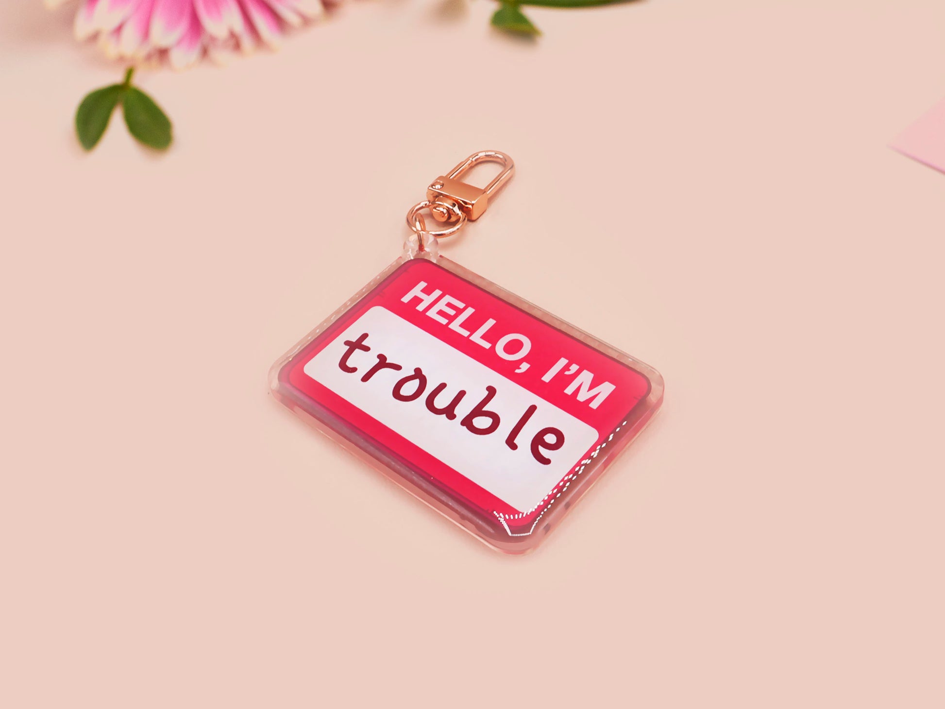 Multiple acrylic keychains with gold swivel clasps in the hello I'm name badge style with the word trouble written instead of a name