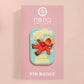 A clear acrylic pin badge with a pink heart-shaped pin back clasp. The design of the pin badge is of a cute chibi retro astronaut floating in sapce with the quote Houston I have so many problems