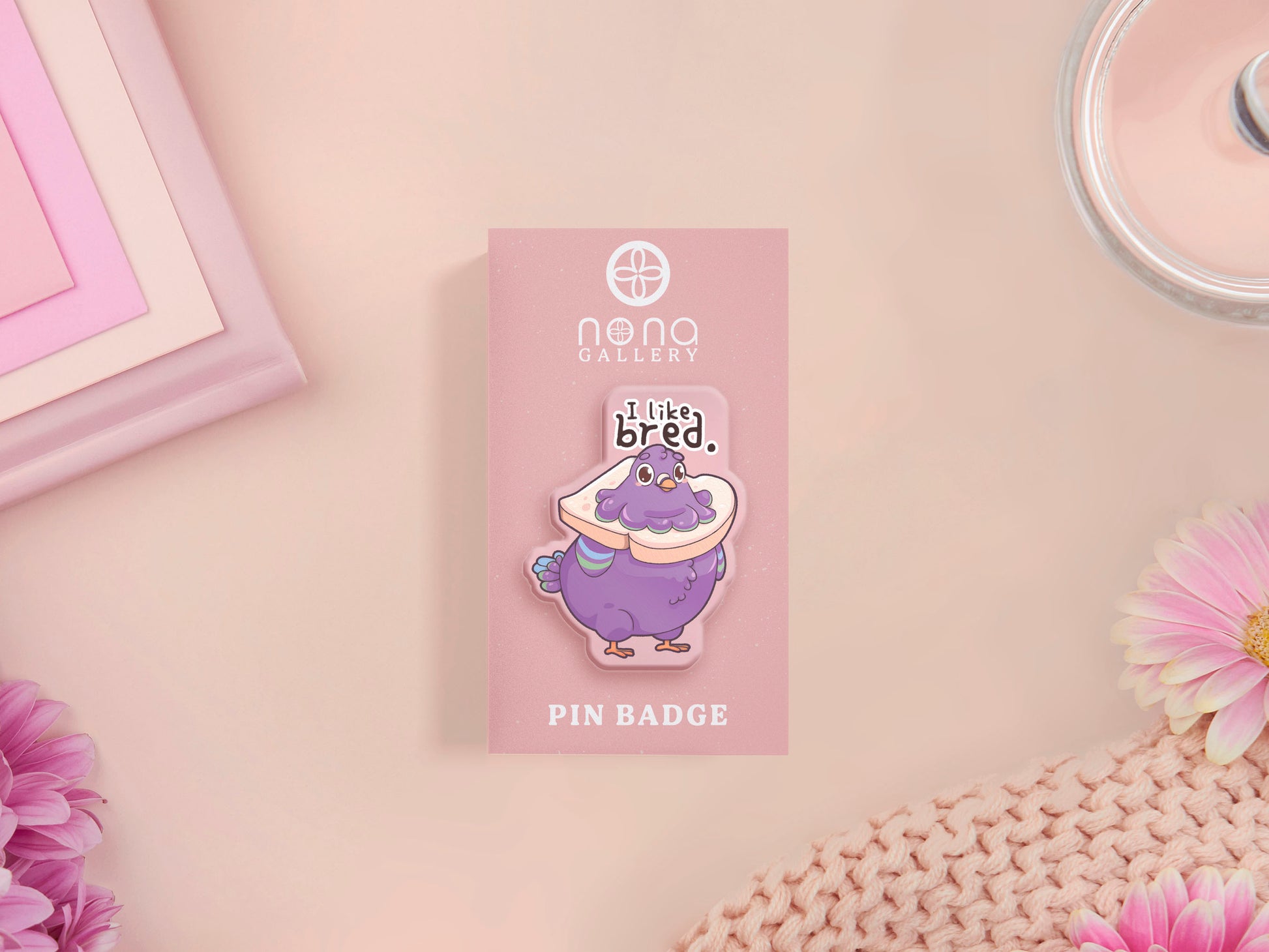 A transparent acrylic pin badge with a pink heart-shaped pin-back clutch. The design of the pin badge is a cute cartoon pigeon with a slice of bread around it's neck with the quote I like bred.