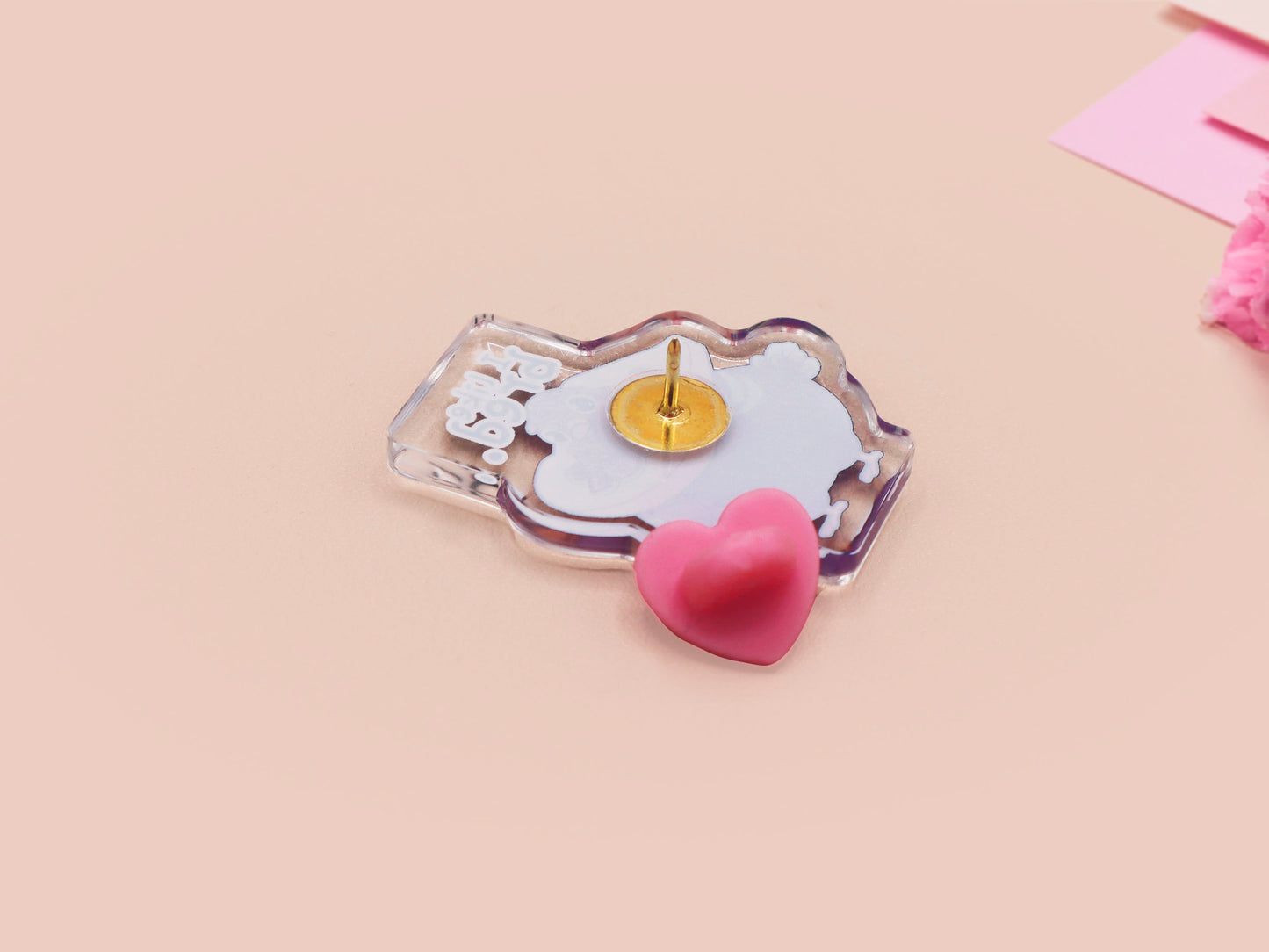 A transparent acrylic pin badge with a pink heart-shaped pin-back clutch. The design of the pin badge is a cute cartoon pigeon with a slice of bread around it's neck with the quote I like bred.