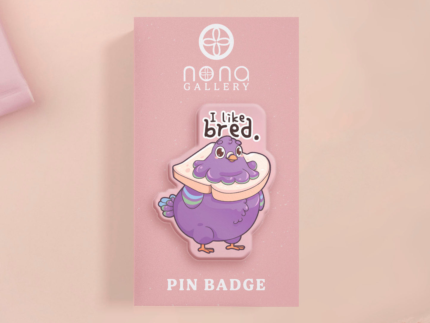 A transparent acrylic pin badge with a pink heart-shaped pin back clutch.The design of the pin badge is a cute cartoon pigeon with a slice of bread around it's neck with the quote I like bred.