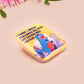 A clear acrylic pin badge with a pink heart-shaped pin back clasp. The design of the pin badge is of a cute chibi blue godzilla like kaiju destroying a city with the quote I Think I Smash Buildings Because My Father Was Distant.