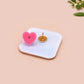 A clear acrylic pin badge with a pink heart-shaped pin back clasp. The design of the pin badge is of a cute chibi blue godzilla like kaiju destroying a city with the quote I Think I Smash Buildings Because My Father Was Distant.