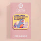 A clear acrylic pin badge with a pink heart-shaped pin back clasp. The design of the pin badge is of a cute chibi blue godzilla like kaiju destroying a city with the quote I Think I Smash Buildings Because My Father Was Distant.