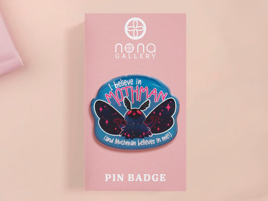 Clear acrylic pin badge with pink heart-shaped rubber pin back clasp. The design of the pin badge is a cute cartoon chibi Mothman cryptid with the quote I believe in Mothman and Mothman believes in me.