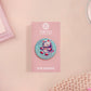 Clear acrylic pin badge with a pink heart-shaped rubber pin back clasp. The design of the pin badge is a cute chibi white cat in a retro astronaut suit with the quote I need space.