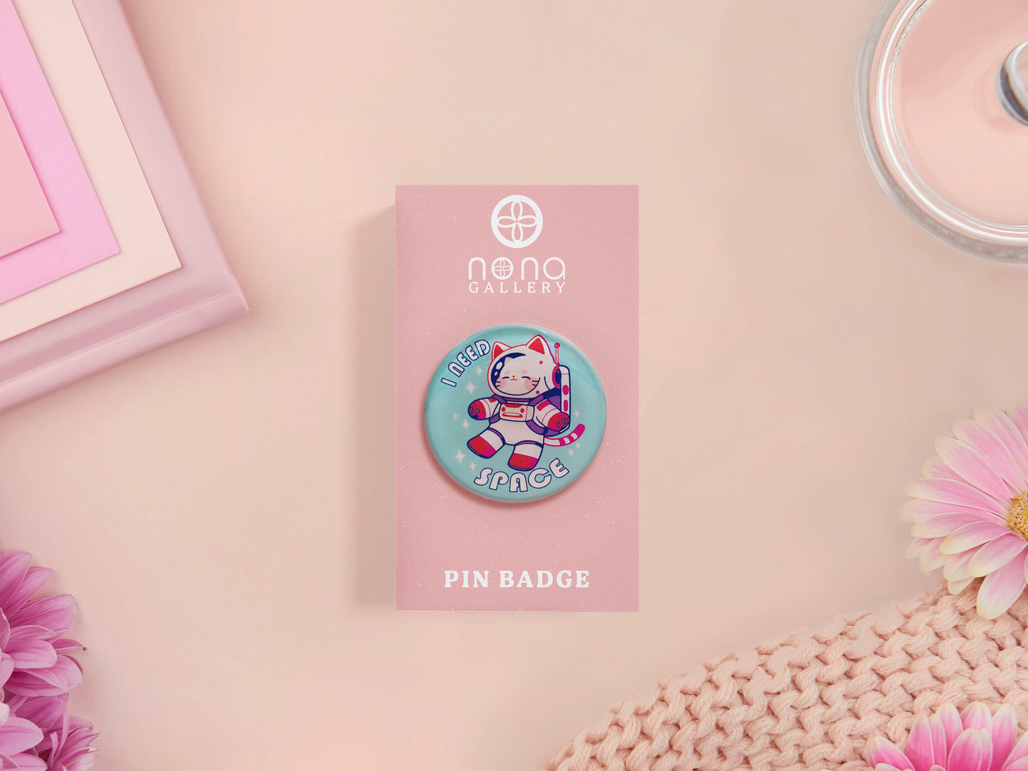 Clear acrylic pin badge with a pink heart-shaped rubber pin back clasp. The design of the pin badge is a cute chibi white cat in a retro astronaut suit with the quote I need space.