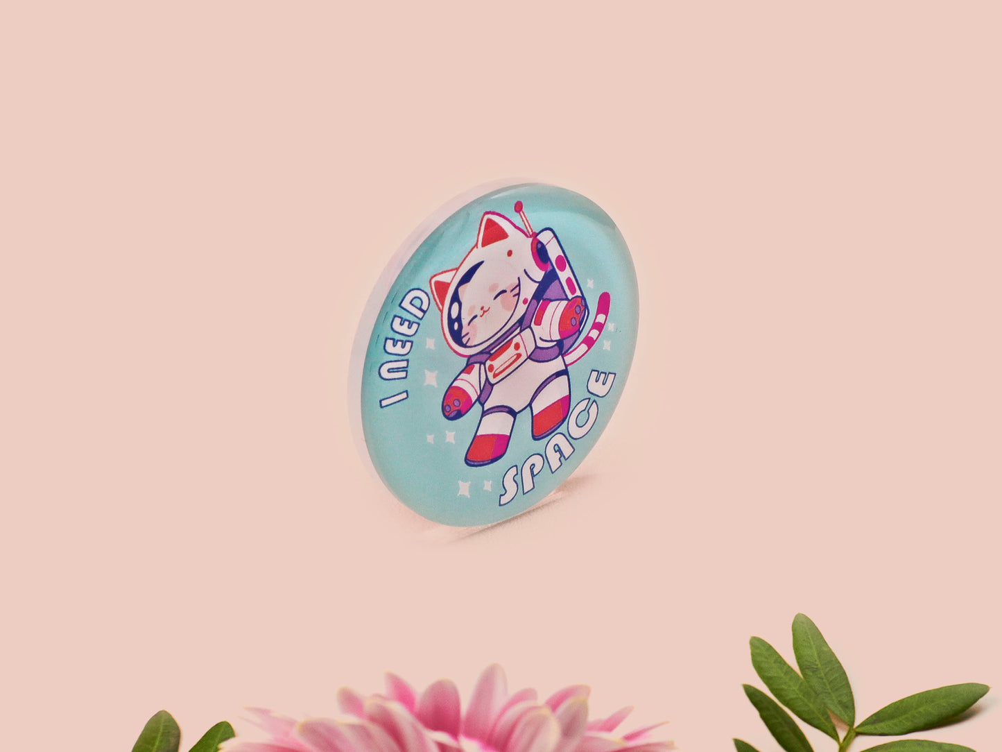Clear acrylic pin badge with a pink heart-shaped rubber pin back clasp. The design of the pin badge is a cute chibi white cat in a retro astronaut suit with the quote I need space.