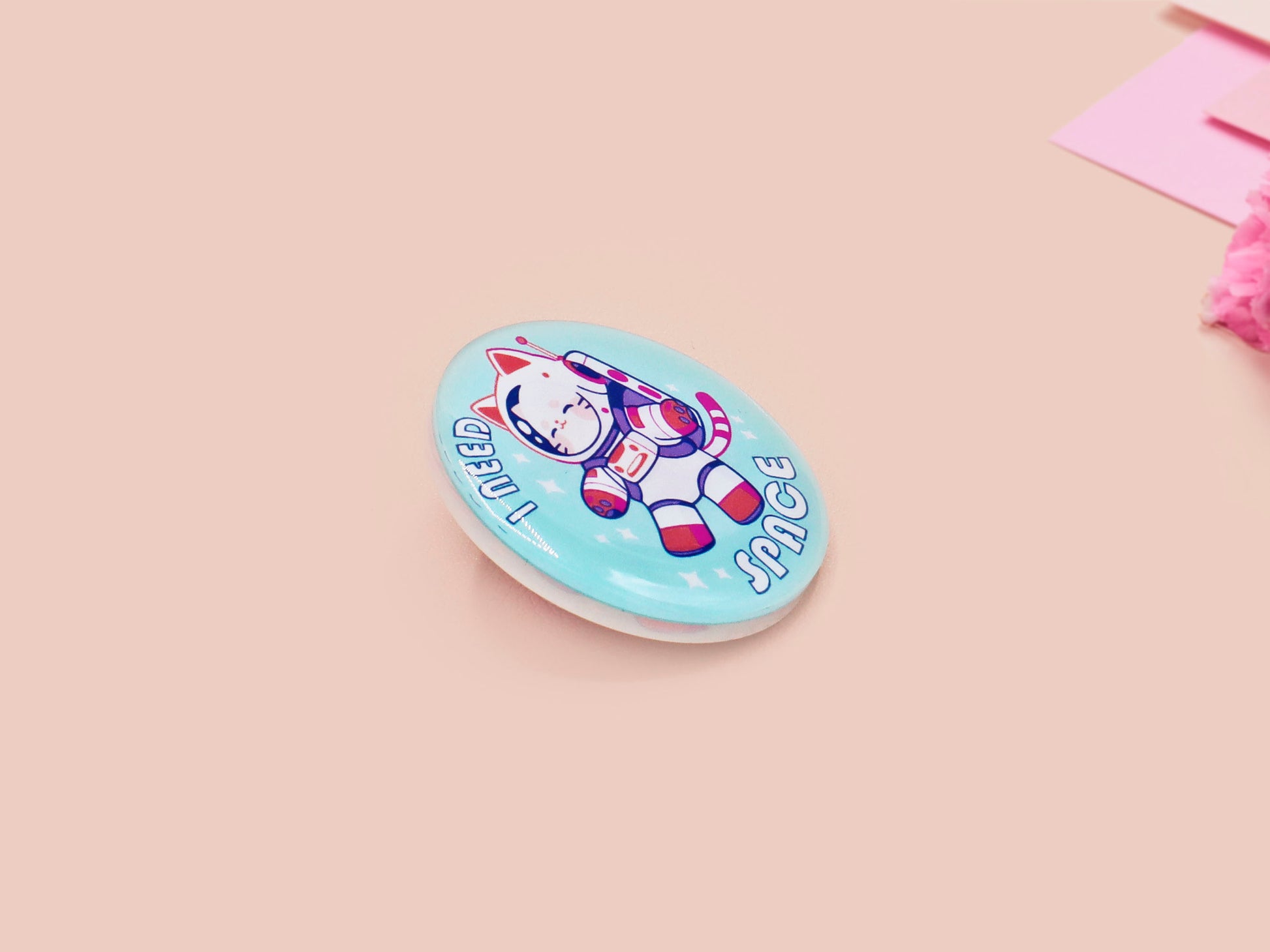 Clear acrylic pin badge with a pink heart-shaped rubber pin back clasp. The design of the pin badge is a cute chibi white cat in a retro astronaut suit with the quote I need space.