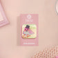 A clear acrylic pin badge with a pink heart-shaped pin back clasp. The design of the pin badge is of a cute chibi pigeon wearing a top hat crying next to a pethetic attempt at nest building with the quote I'm trying my best.