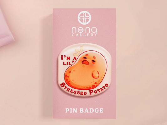 A clear acrylic pin badge with a pink heart-shaped pin back clasp. The design of the pin badge is of a cute chibi potato with the quote I'm a lil' stressed potato