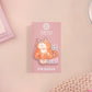 Clear acrylic pin badge with pin heart-shaped pin back clasp. The design of the pin badge is a cute cartoon ginger cat sat in a small cardboard box with the quote if I fits I sits.