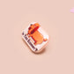 A clear acrylic pin badge with a pink heart-shaped pin back clasp. The design of the pin badge is of a cute chibi dachshund sausage dog with the quote in this economy?