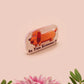 A clear acrylic pin badge with a pink heart-shaped pin back clasp. The design of the pin badge is of a cute chibi dachshund sausage dog with the quote in this economy?