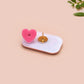 A clear acrylic pin badge with a pink heart-shaped pin back clasp. The design of the pin badge is of a cute chibi dachshund sausage dog with the quote in this economy?