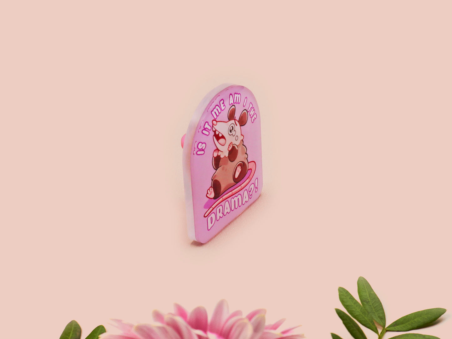 A clear acrylic pin badge with a pink heart-shaped pin back clasp. The design of the pin badge is of a cute screaming possum with the quote is it me am I the drama?