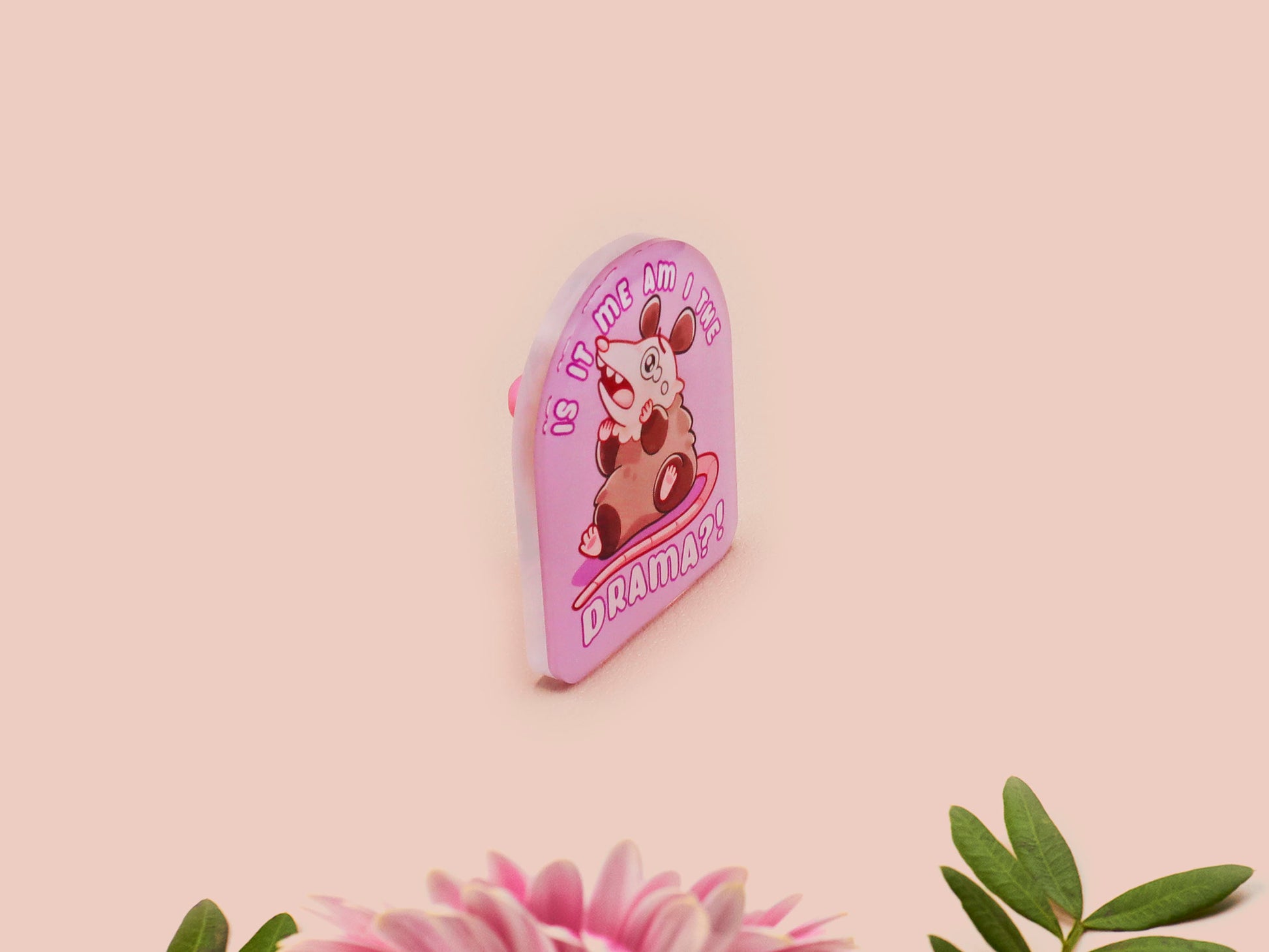 A clear acrylic pin badge with a pink heart-shaped pin back clasp. The design of the pin badge is of a cute screaming possum with the quote is it me am I the drama?