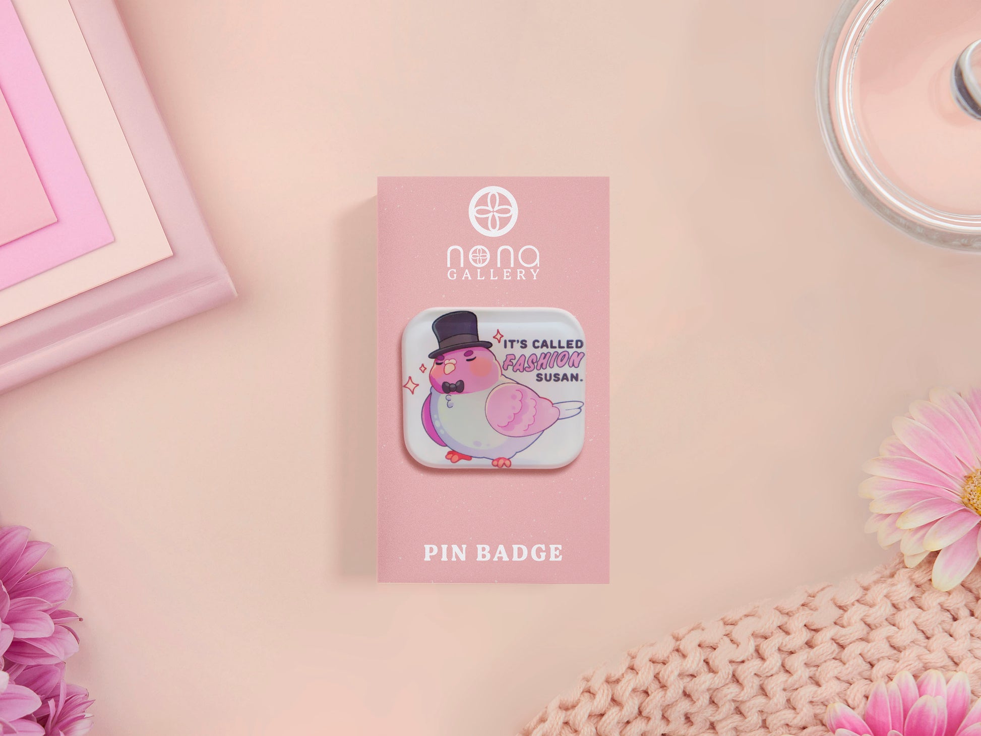 A clear acrylic pin badge with a pink heart-shaped pin back clasp. The design of the pin badge is of a cute chibi pigeon wearing a top hat with the quoteit's called fashion susan