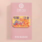 A clear acrylic pin badge with a pink heart-shaped pin back clasp. The design of the pin badge is of a cute chibi blue godzilla like kaiju mothra and King Ghidorah destroying a city with the quote kaiju fanclub and kaiju warning in japanese kanji