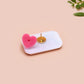 A clear acrylic pin badge with a pink heart-shaped pin back clasp. The design of the pin badge is of a cute chibi blue godzilla like kaiju mothra and King Ghidorah destroying a city with the quote kaiju fanclub and kaiju warning in japanese kanji
