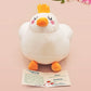 An adorable white duck bird plushie toy with cute embroidered eyes and facial expression, wearing a yellow crown hat, with a hang tag describing the duck as King Larry.